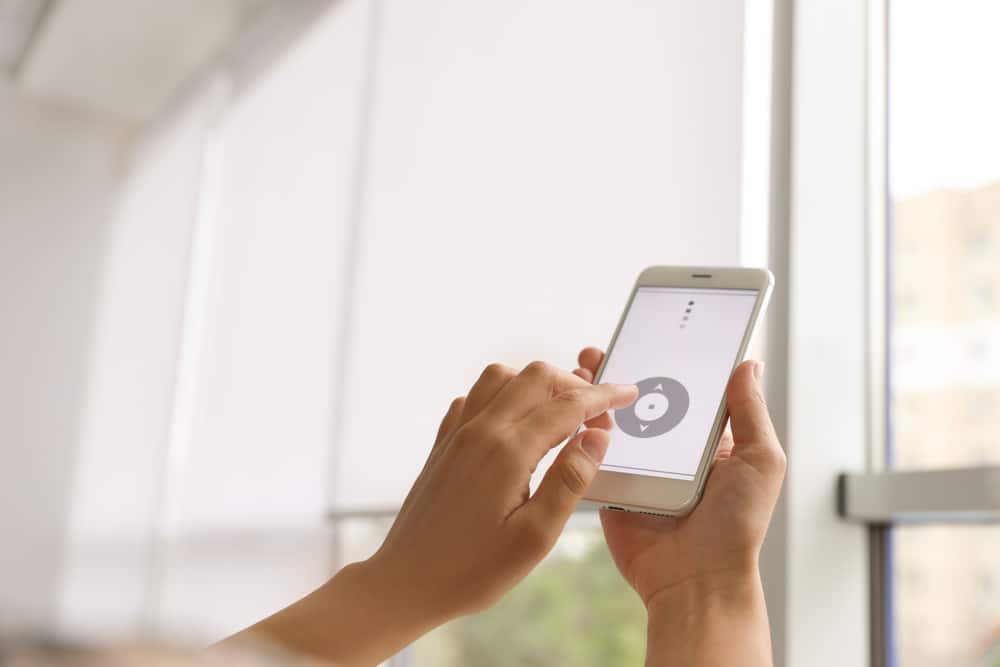 Woman using smart home application on phone to control smart window shades and blinds.