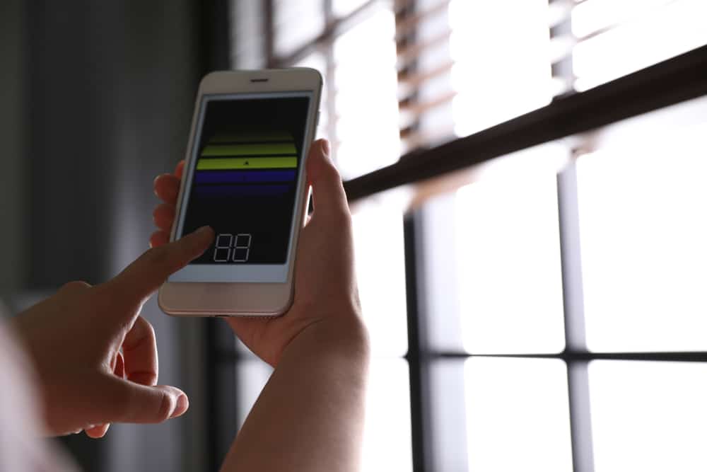 Woman using smart home application on phone to control smart window shades and blinds.