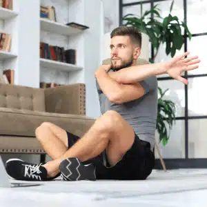 Man doing shoulder stretches in a living room, possibly using the best home gym speakers