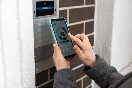Person uses smartphone to unlock entry system, demonstrating how intercom works remotely today