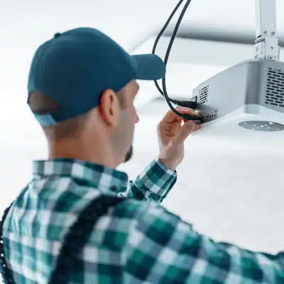 A technician adjusts cables on a ceiling-mounted projector to ensure a high-quality home theater experience