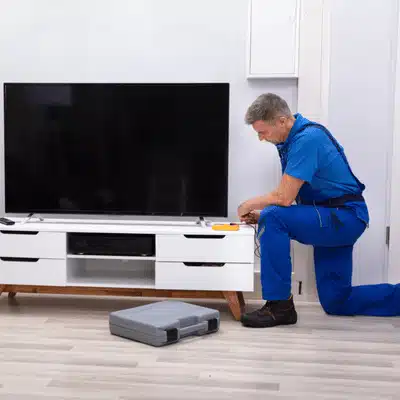 Professional technician kneels to connect wires to a large flat-screen TV in a modern home