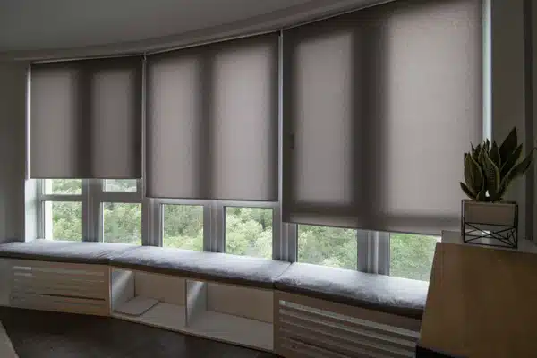 Grey roller shades cover curved windows above bench seating, reducing glare and enhancing privacy indoors