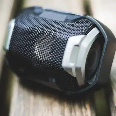 Close-up of wireless outdoor speakers with black mesh design placed on a wooden bench outdoors