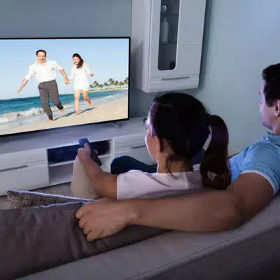 Couple watches large television in living room, considering projector vs tv for home entertainment upgrade