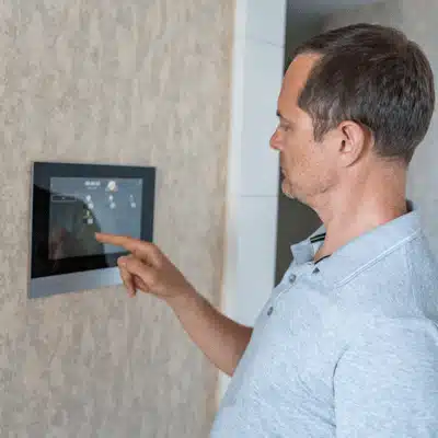 Person uses wall-mounted smart home control panel, adjusting lights and temperature settings inside house today