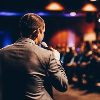 Presenter speaking into microphone before crowd at event; church sound system installation supports clear audio