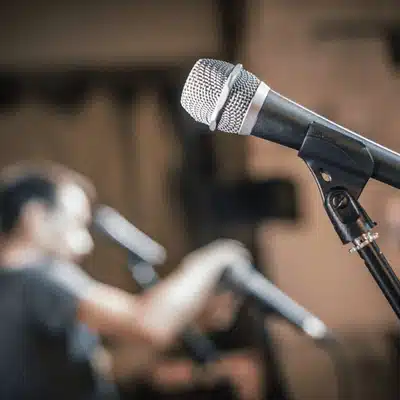 Microphone on stand in church, technician blurred behind; church sound system installation rehearsal setup shown