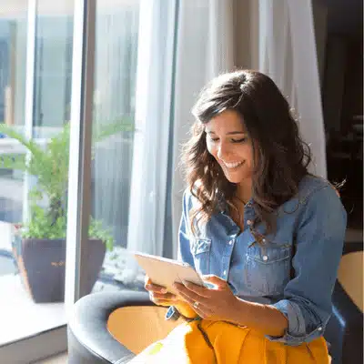 Photo shows happy woman using tablet to manage devices installed by home technology integrators remotely