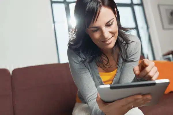 Photo shows smiling woman on sofa using tablet, enjoying systems installed by home technology integrators