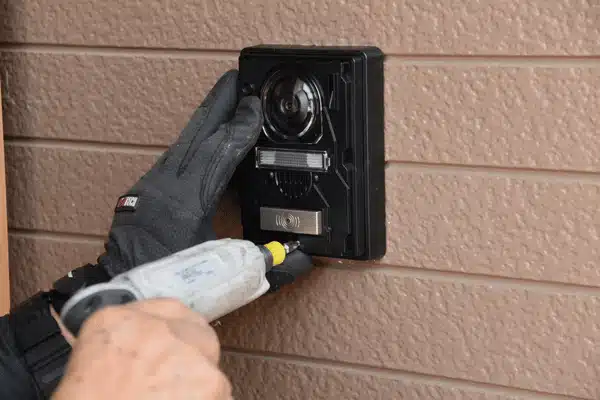 Technician mounts video door unit with drill while intercom systems for home improve entry security