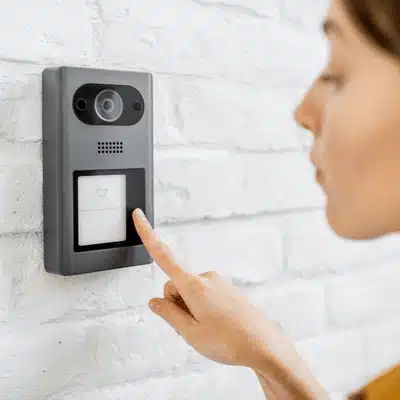 Person presses wall-mounted video door unit button, demonstrating Wireless home intercom systems entry control