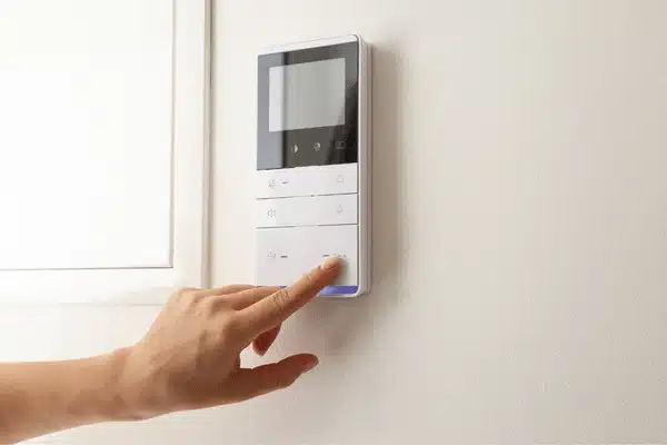 Finger presses wall-mounted intercom panel, demonstrating Intercom systems for home for secure entry communication today