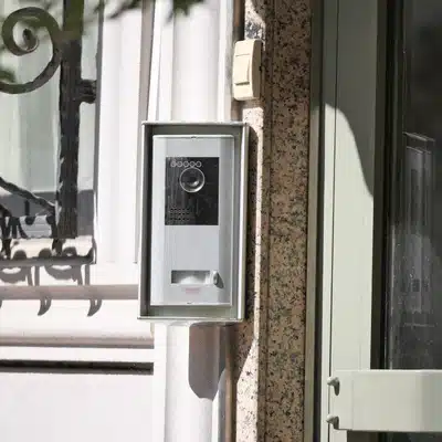 A wall-mounted outdoor video intercom sits beside a home entrance, representing wireless home intercom systems for visitor screening