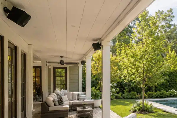 Patio Speaker Setup Outdoor speakers are mounted beneath the ceiling of a covered backyard patio overlooking a landscaped garden and swimming pool